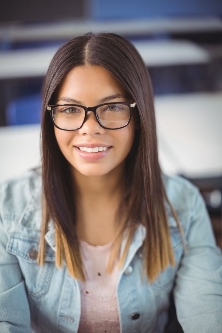 Hispanic Teenage Girl Smiling in Classroom with Denim Jacket and Glasses
