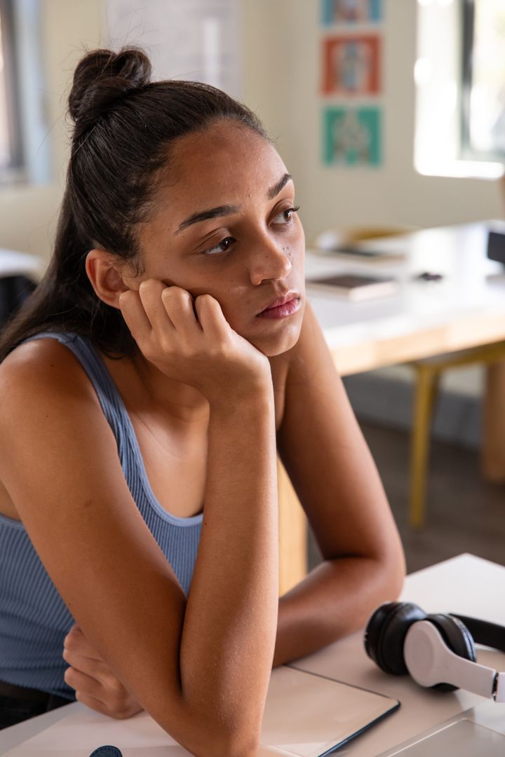 Pensive teenage girl studying at desk with notebook and headphones, looking distracted