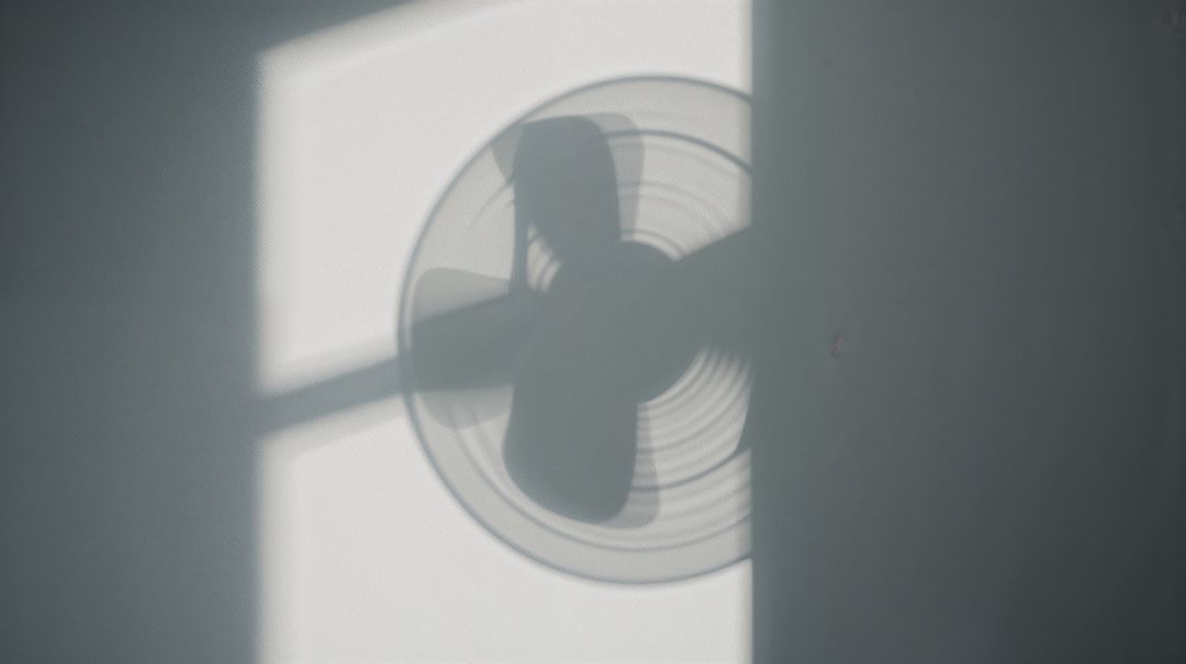 Casting Fan Shadow Overlapping Human Silhouette on Sunlit Wall with Geometric Window Light