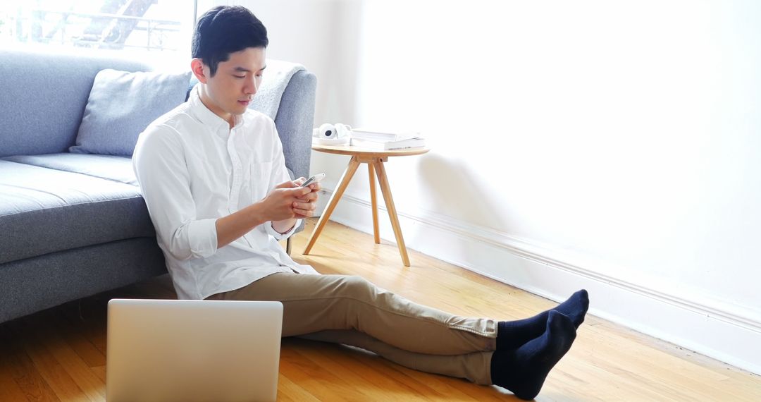 Man Sitting on Floor Next to Sofa Using Smartphone in Bright Living Room - Free Images, Stock Photos and Pictures on Pikwizard.com