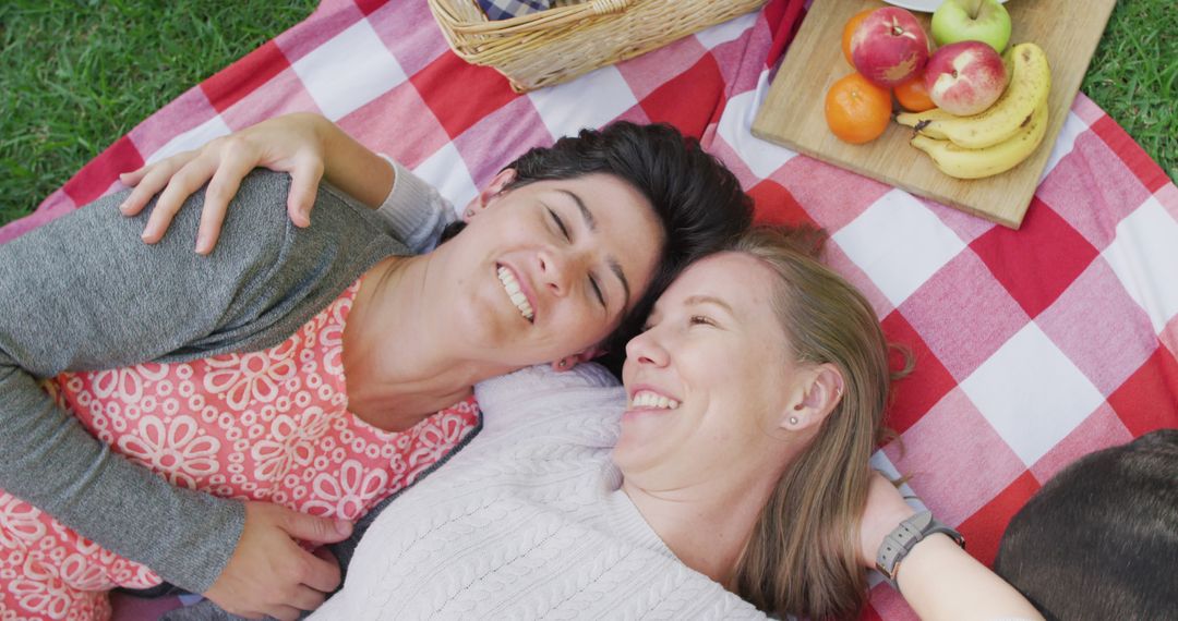 Overhead view of caucasian lesbian couple lying on the blanket in the garden during picnic - Free Images, Stock Photos and Pictures on Pikwizard.com