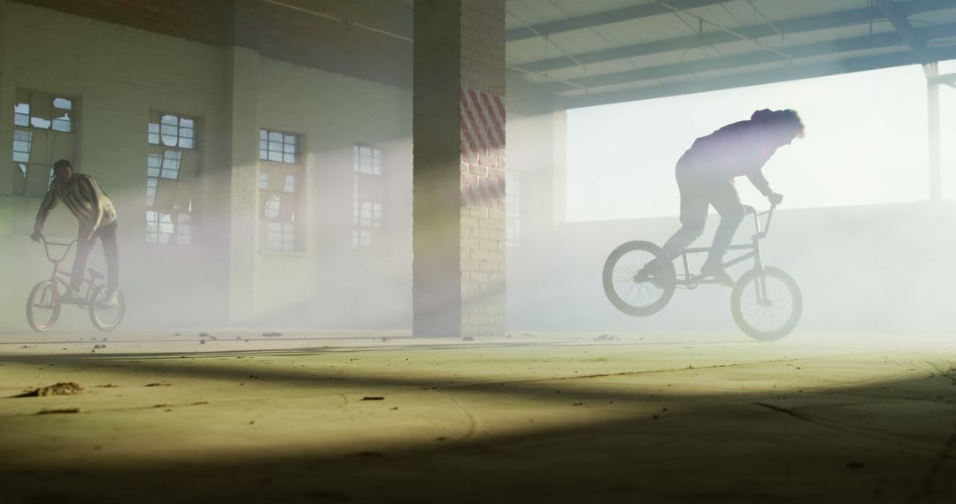 BMX Cyclists Performing Tricks in Abandoned Warehouse with Sunlight - Free Images, Stock Photos and Pictures on Pikwizard.com