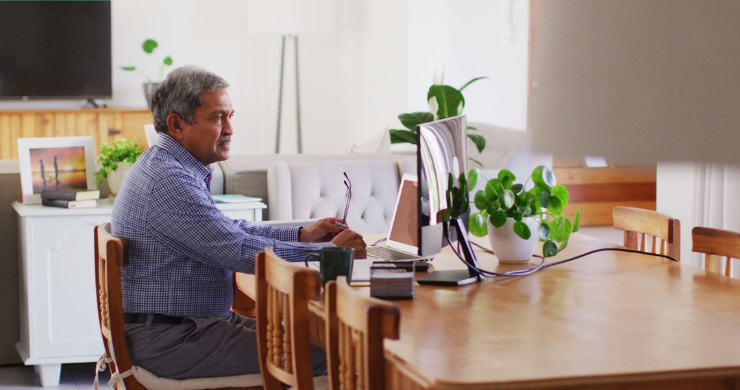 Image of senior biracial man sitting at dining table using computer - Free Images, Stock Photos and Pictures on Pikwizard.com