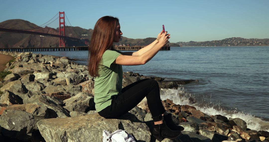 Young Woman Taking Selfie on Rocky Beach with Golden Gate Bridge in Background - Free Images, Stock Photos and Pictures on Pikwizard.com