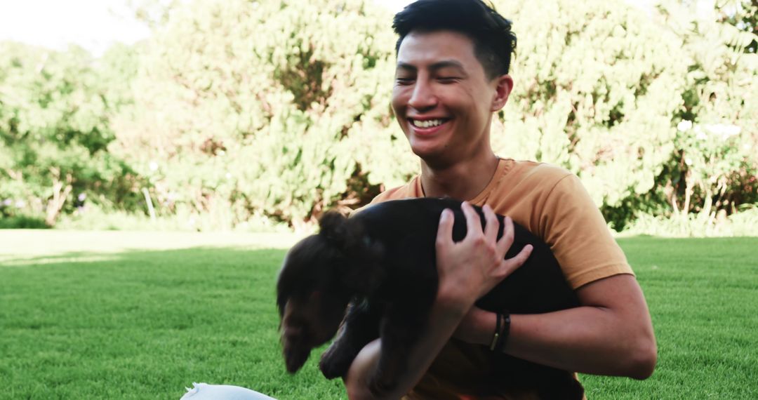 Cheerful Young Man Relaxing with Puppy in Sunny Park