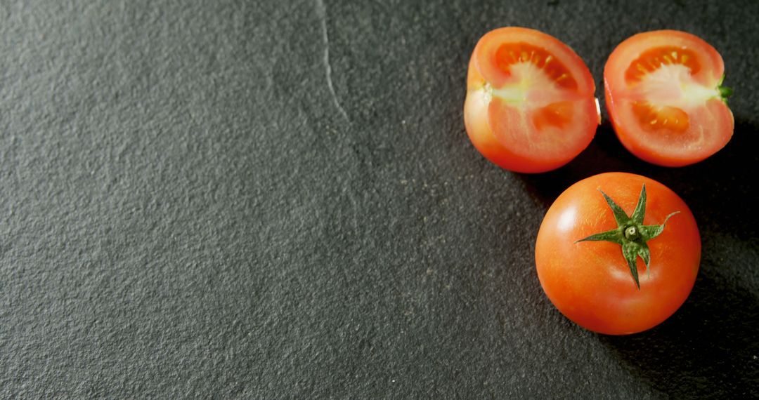 Fresh red tomatoes are halved and whole on a dark slate surface, with copy space - Free Images, Stock Photos and Pictures on Pikwizard.com