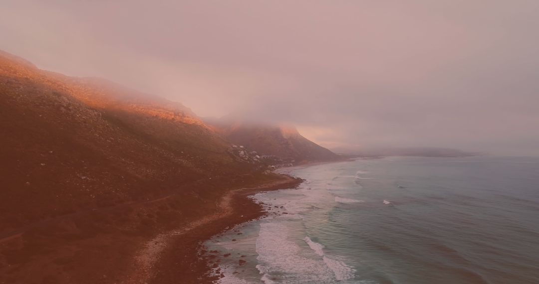 Misty Coastal View with Ocean Waves and Mountains at Sunset