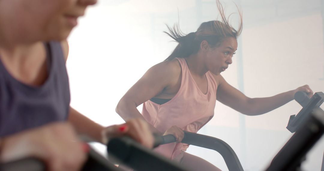 Two Women Actively Exercising on Stationary Bikes - Free Images, Stock Photos and Pictures on Pikwizard.com