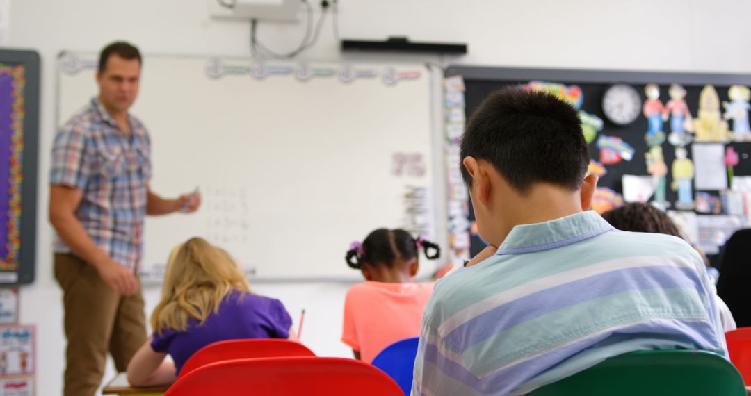 Children Focused in Classroom with Male Teacher Nearby Whiteboard