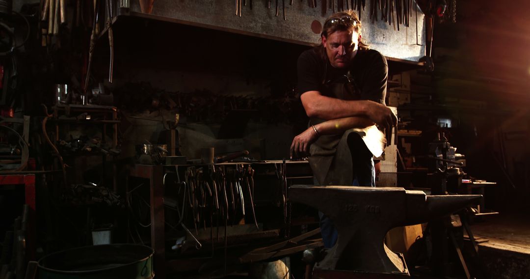 Blacksmith resting after working in dark forge workshop illuminated by soft warm light - Free Images, Stock Photos and Pictures on Pikwizard.com