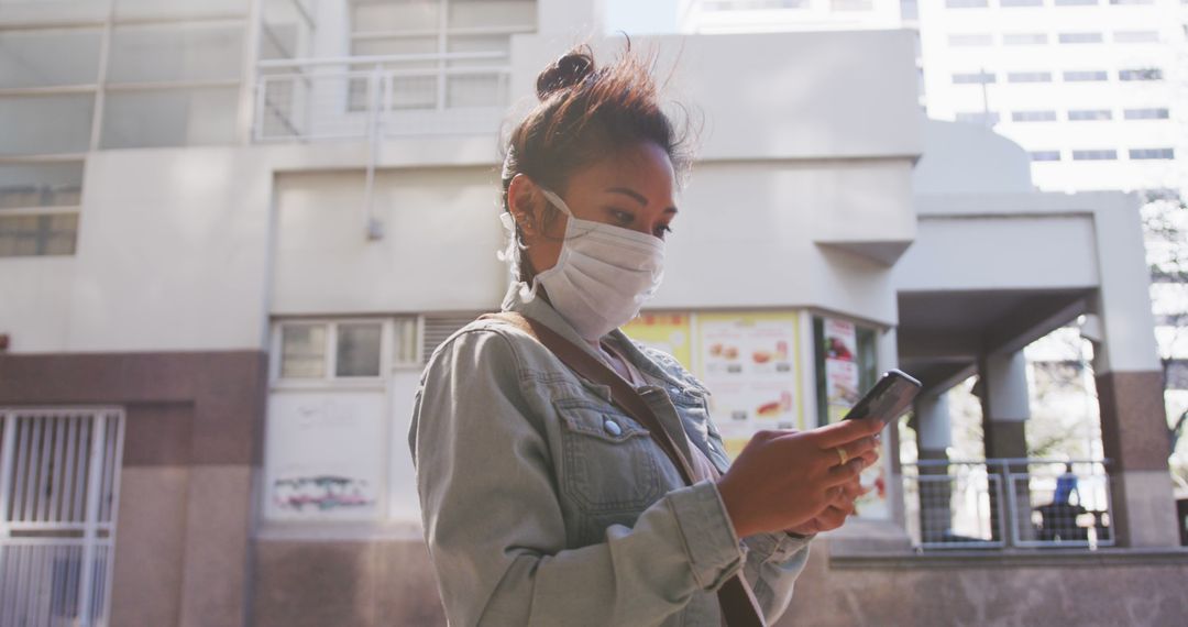 Asian woman wearing mask using smartphone outdoors in urban area - Free Images, Stock Photos and Pictures on Pikwizard.com