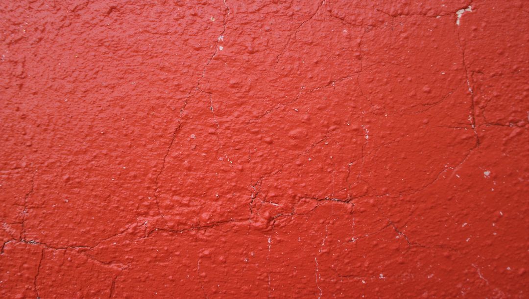 Cracked red stucco wall revealing lighter substrate, textured paint peeling and fissures