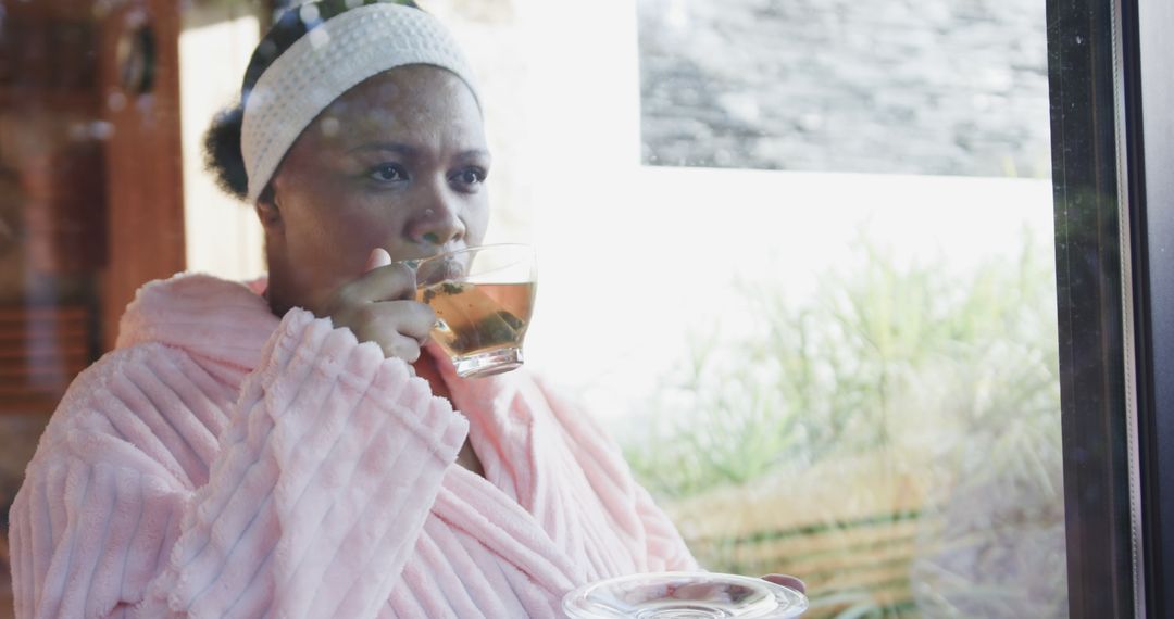 Woman in pink robe drinking tea by window - Free Images, Stock Photos and Pictures on Pikwizard.com