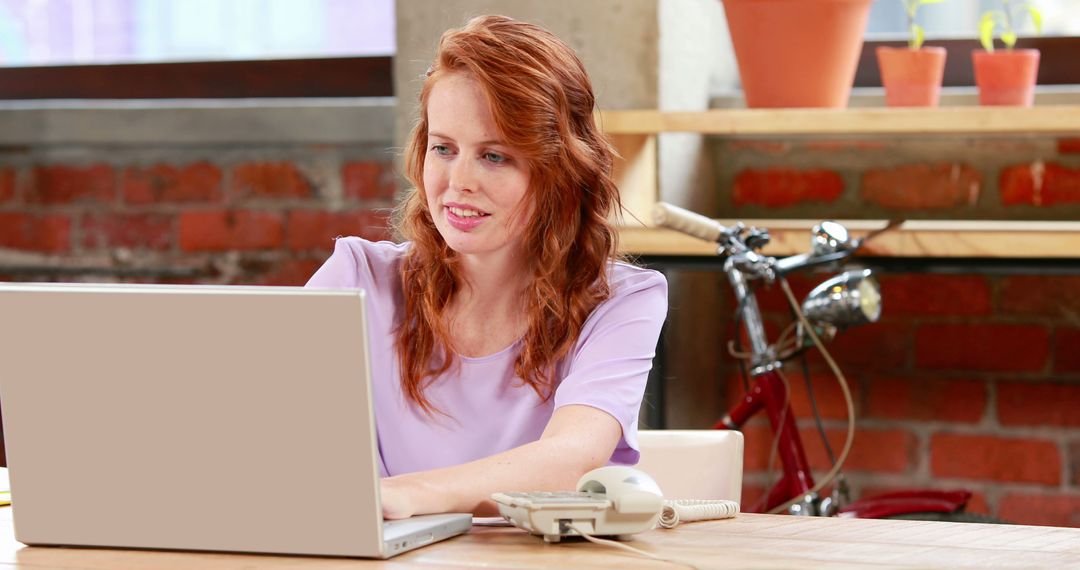 Redhead Woman Working on Laptop in Modern Office Setting - Free Images, Stock Photos and Pictures on Pikwizard.com