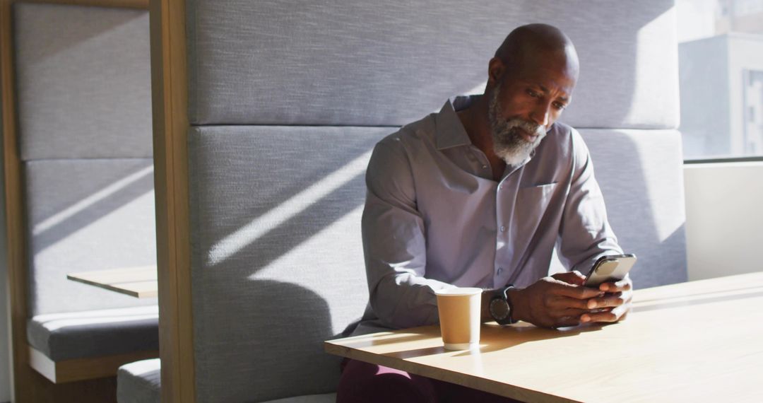Man Relaxing at Cafe Inspects Smartphone in Sunny Booth