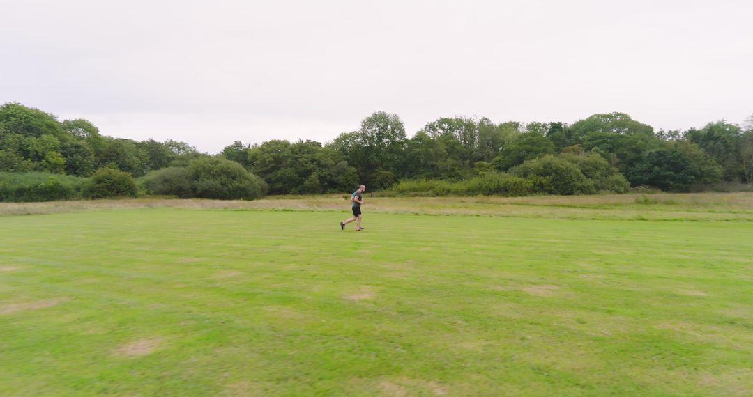 Couple Jogging on Green Field Surrounded by Lush Trees