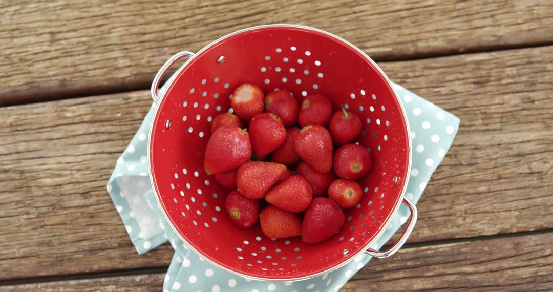 A red colander filled with fresh strawberries sits on a wooden surface, with copy space - Free Images, Stock Photos and Pictures on Pikwizard.com