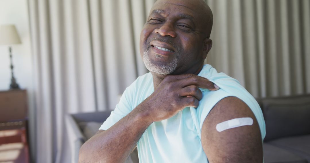 Smiling Senior Man Showing Arm with Vaccine Bandage Indoors - Free Images, Stock Photos and Pictures on Pikwizard.com