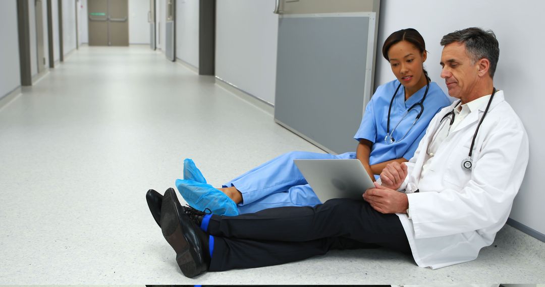 Doctors Sitting on Hospital Floor Discussing Over Tablet in Hallway - Free Images, Stock Photos and Pictures on Pikwizard.com