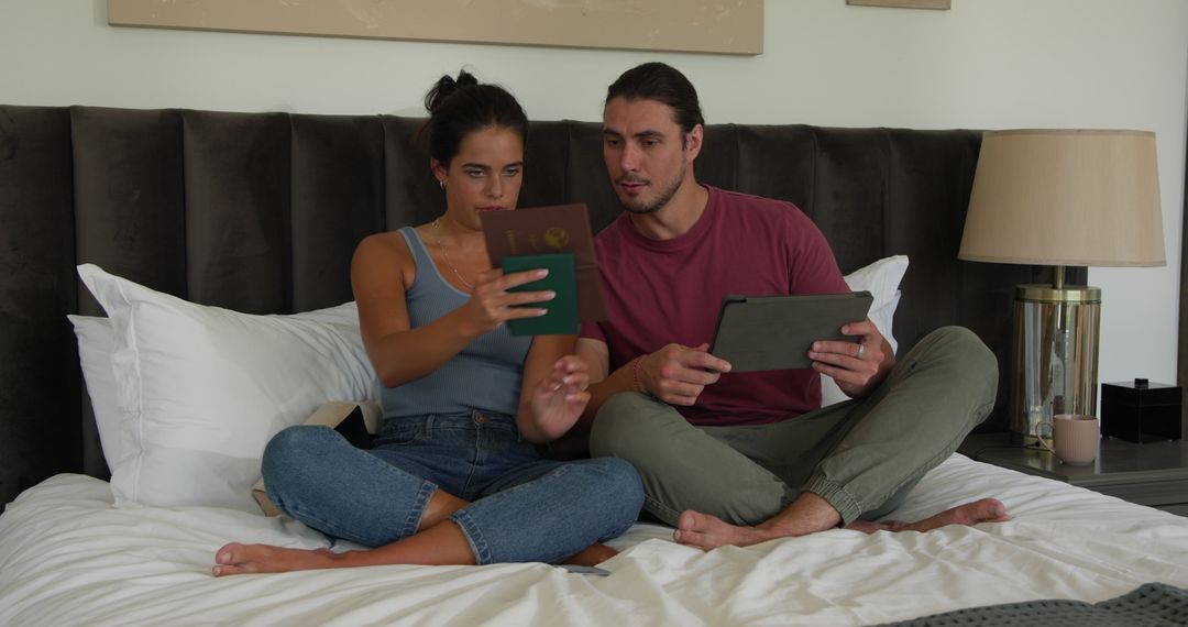 Couple Planning Trip Using Passports and Tablet on Bed