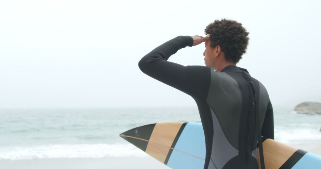 Surfer Gazing at Ocean While Holding Surfboard on Beach