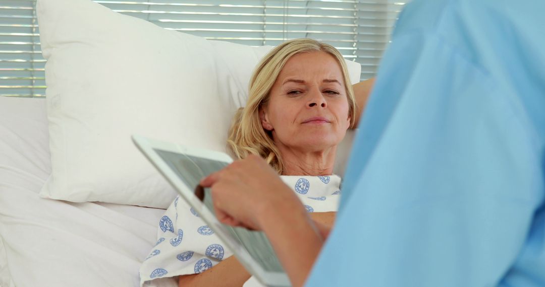 A middle-aged Caucasian woman in a hospital gown is looking at a digital tablet, with copy space - Free Images, Stock Photos and Pictures on Pikwizard.com