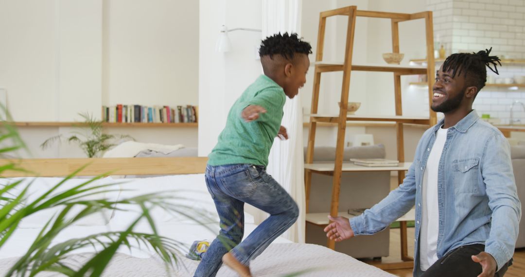 Child jumping on bed while father watches and smiles in cozy home - Free Images, Stock Photos and Pictures on Pikwizard.com