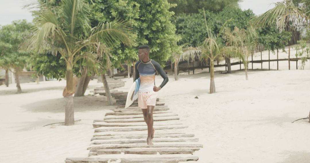 Young Man Walking on Wooden Path Towards Beach with Surfboard - Free Images, Stock Photos and Pictures on Pikwizard.com