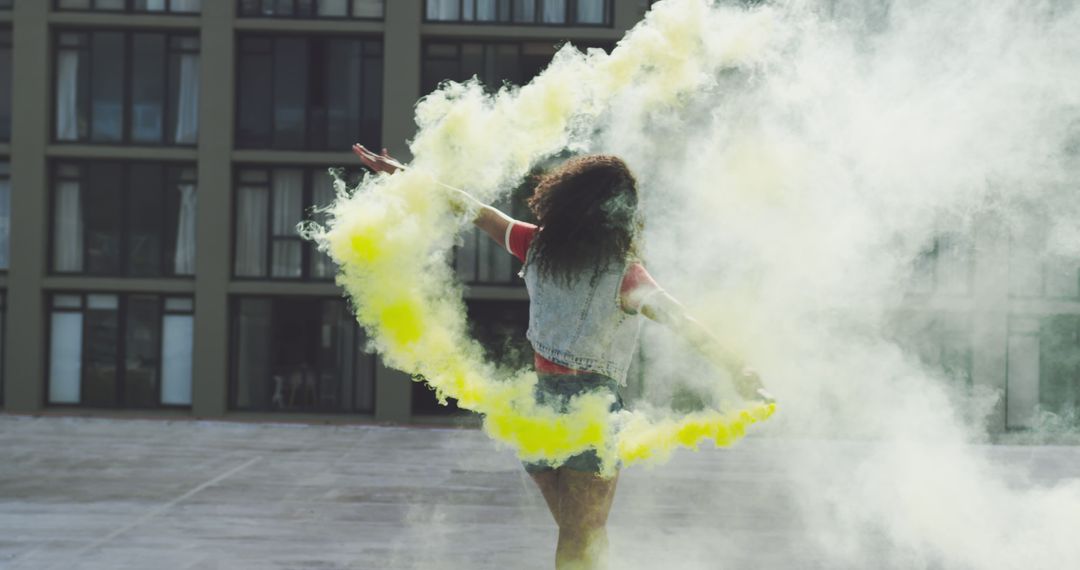 Young biracial woman dances amidst vibrant yellow smoke outdoors - Free Images, Stock Photos and Pictures on Pikwizard.com
