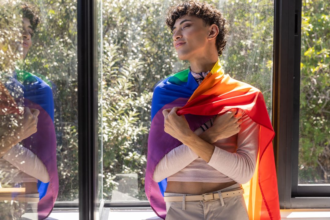 Pride and Self-Love: Man Draped in Rainbow Flag Near Window
