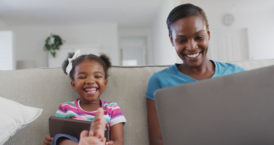 Happy African American Mother and Daughter Using Devices on Couch at Home - Free Images, Stock Photos and Pictures on Pikwizard.com