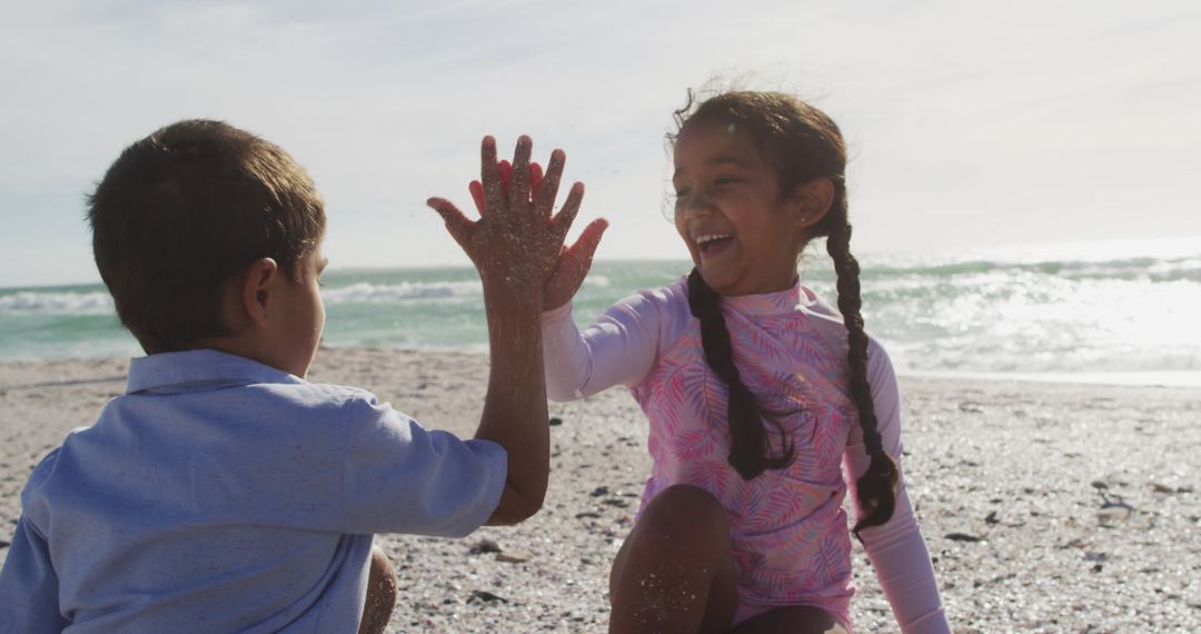 Joyful Hispanic Siblings Playing and High-fiving on Sunny Beach