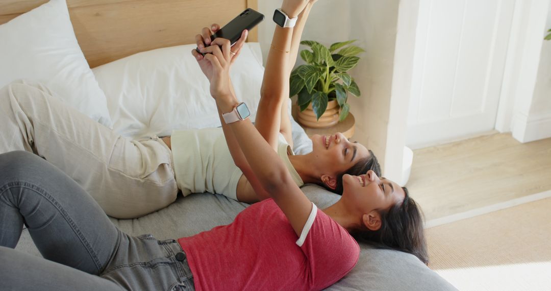 Diverse Women Friends Using Smartphone Relaxing On Bed
