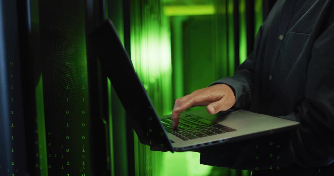 IT Technician Operating Laptop in Data Center with Green LED Lights