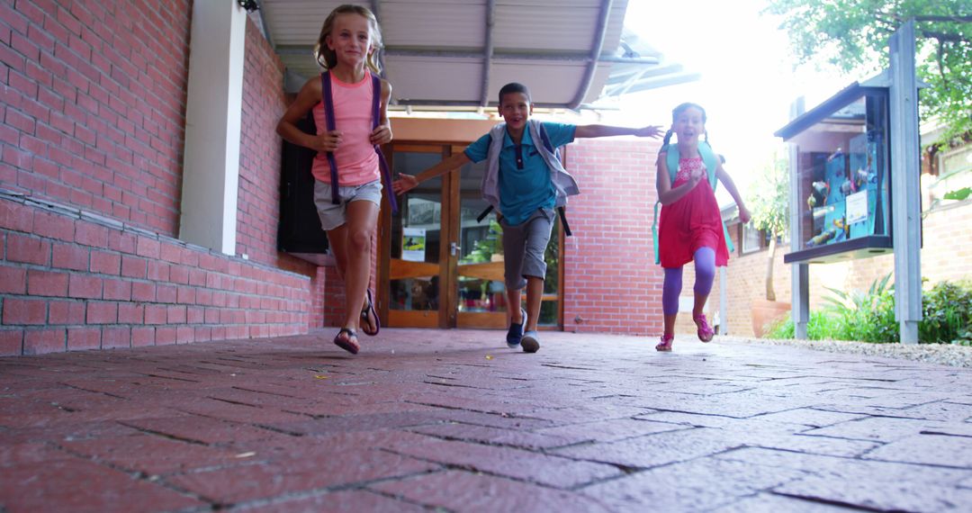 Joyful Students Running in School Corridor Holding Backpacks