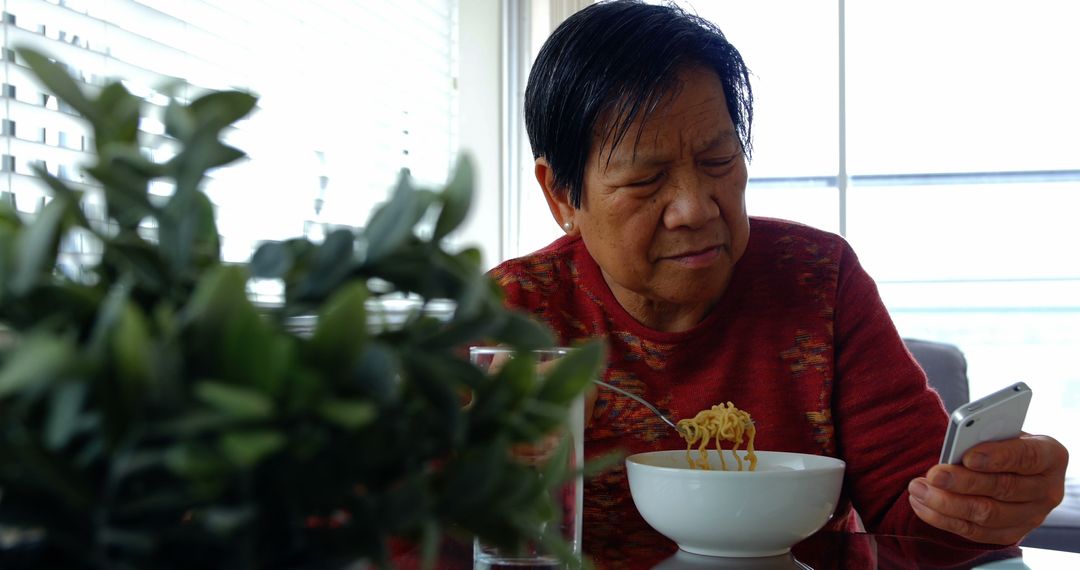 Senior Woman Enjoying Noodles at Home While Using Smartphone - Free Images, Stock Photos and Pictures on Pikwizard.com