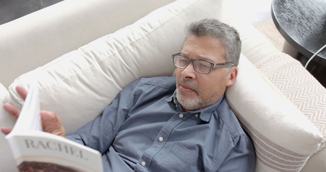 Middle-aged man reading book on couch, relaxing at home - Free Images, Stock Photos and Pictures on Pikwizard.com