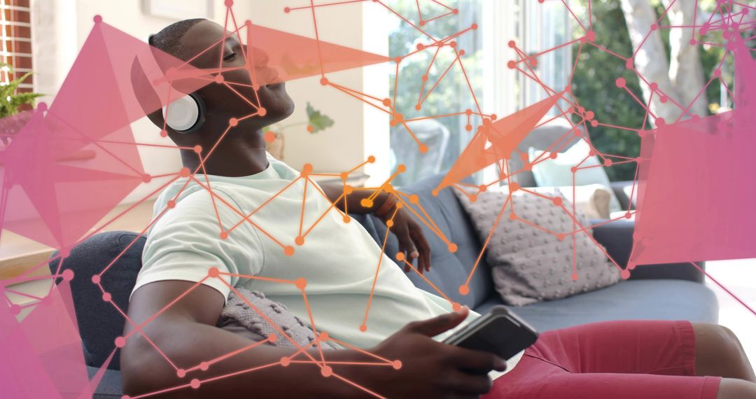 Man relaxing on sofa listening to music with headphones holding smartphone and streaming