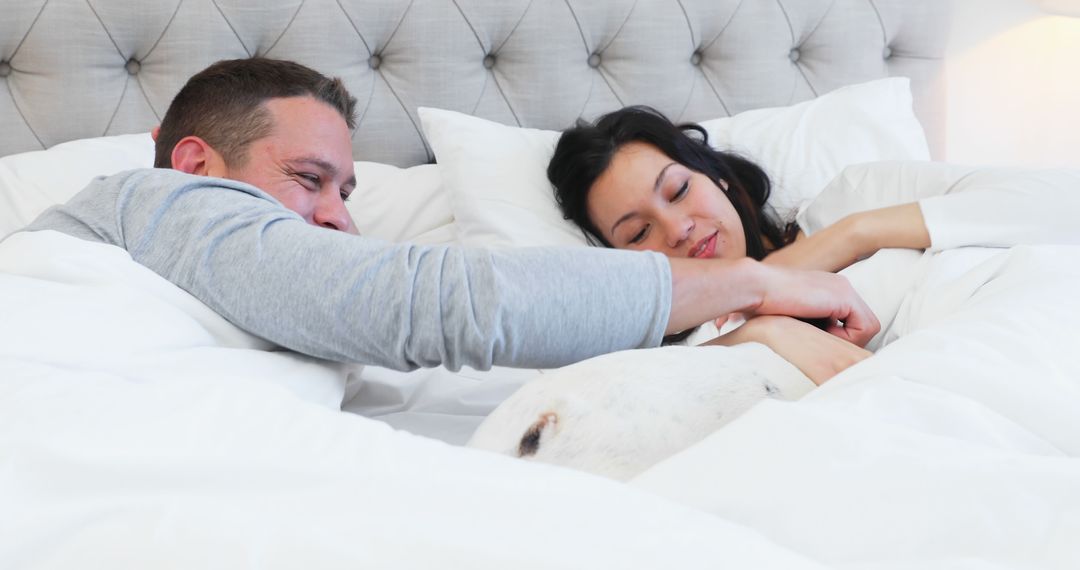 Mixed Race Couple Relaxing in Bed with Dog Enjoying Morning