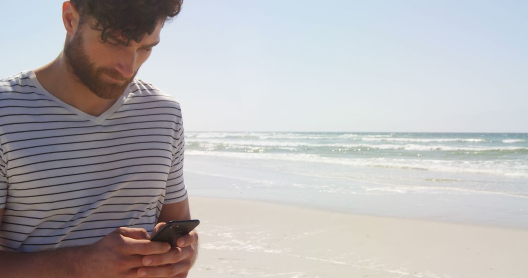 Young Man Focusing on Smartphone on Sandy Beach Location - Free Images, Stock Photos and Pictures on Pikwizard.com