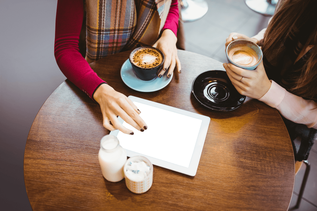 Women Using Transparent Tablet in Cafe with Coffee Cups and Milk