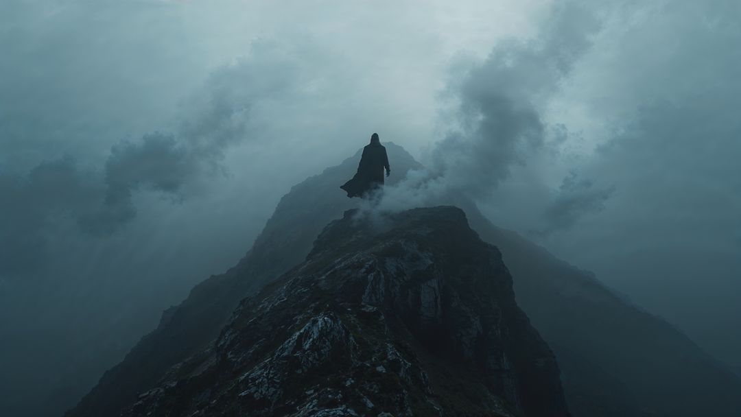 Hooded assassin figure overlooking misty valley on jagged mountain ridge