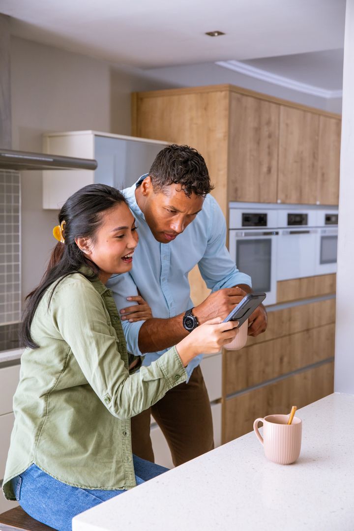 Diverse Couple Reviewing Credit Card Transaction on Smartphone at Kitchen