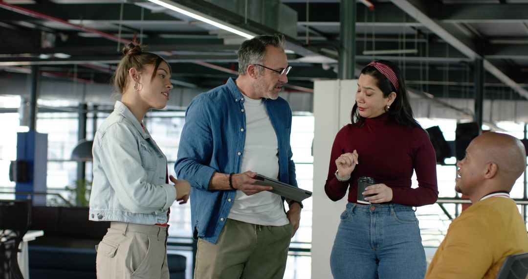 Multicultural team collaborating in modern open-plan workspace with tablet and coffee