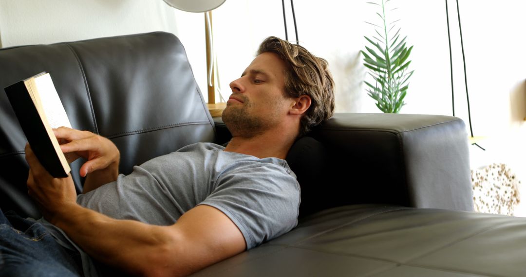 Young Man Relaxing on Leather Sofa While Reading Book - Free Images, Stock Photos and Pictures on Pikwizard.com