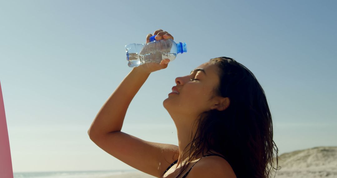 Young Woman Drinking Water on Sunny Beach - Free Images, Stock Photos and Pictures on Pikwizard.com