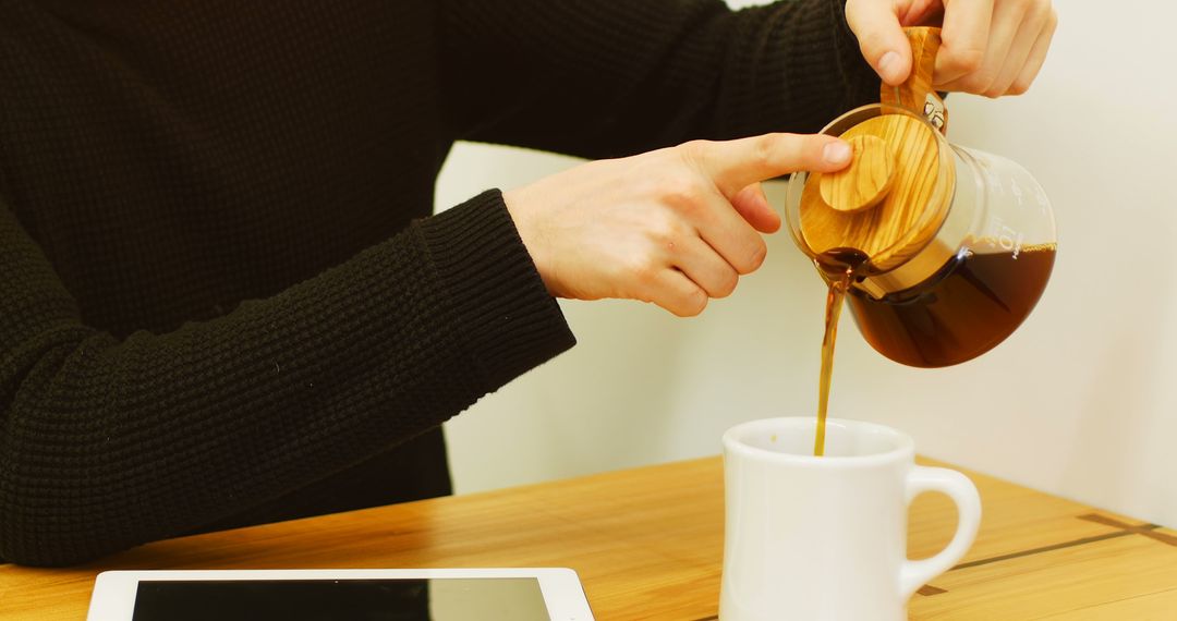 Person Pouring Coffee from Carafe into Cup Beside Tablet - Free Images, Stock Photos and Pictures on Pikwizard.com