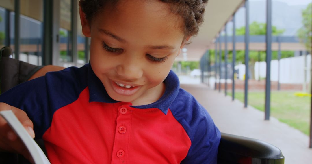 Smiling Child Reading in Wheelchair in School Corridor