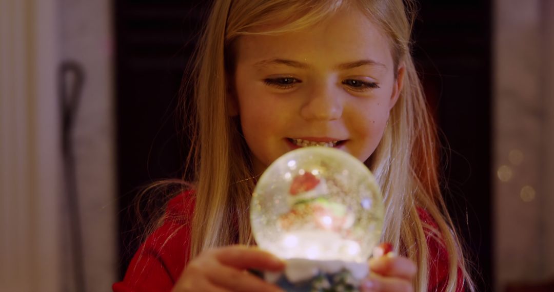 Young Girl Fascinated by Sparkling Snow Globe Indoors