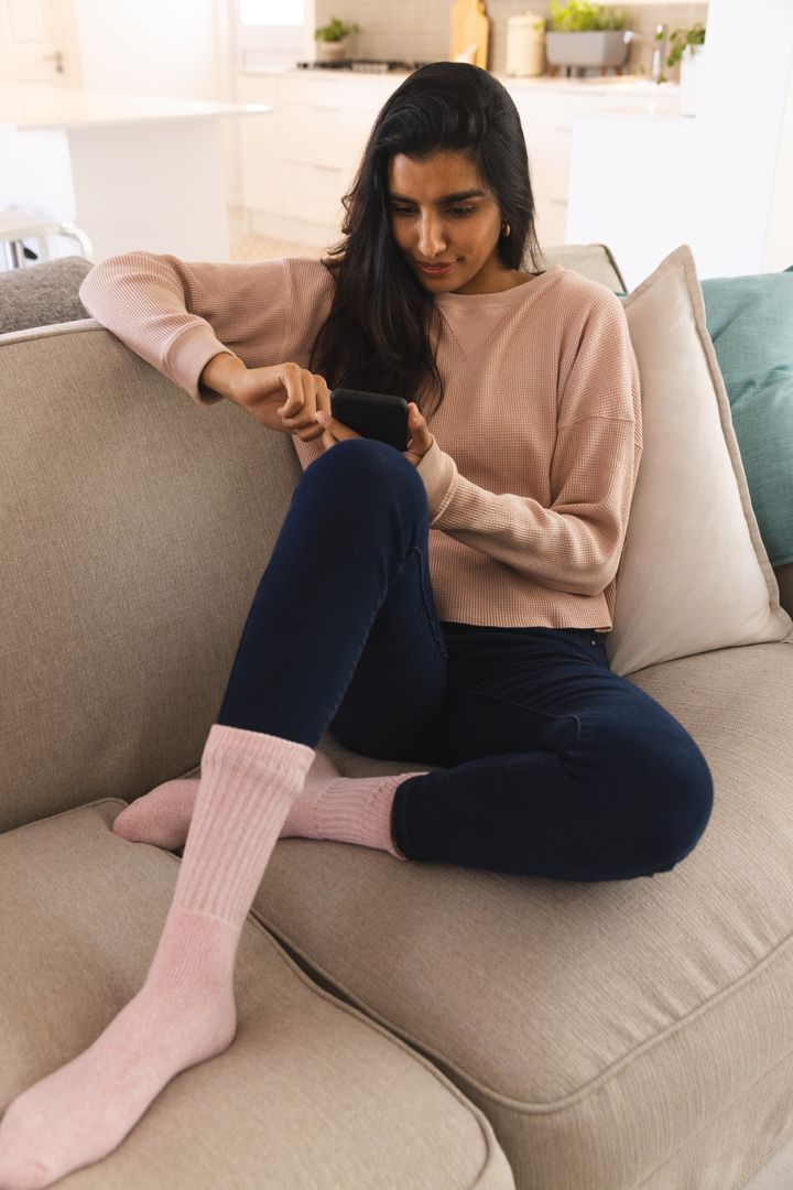 Woman Relaxing on Cozy Couch Using Smartphone at Home